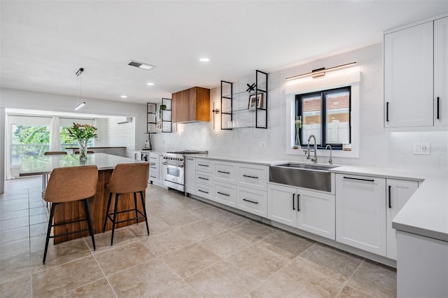 kitchen featuring a breakfast bar, sink, white cabinetry, high end range, and pendant lighting