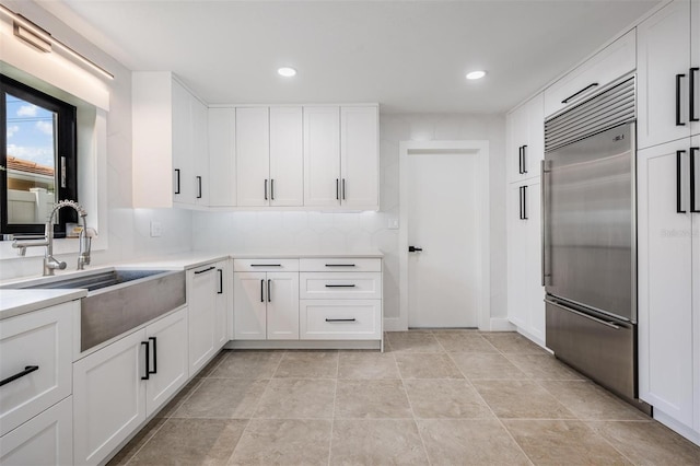 kitchen with built in fridge, white cabinetry, sink, and tasteful backsplash