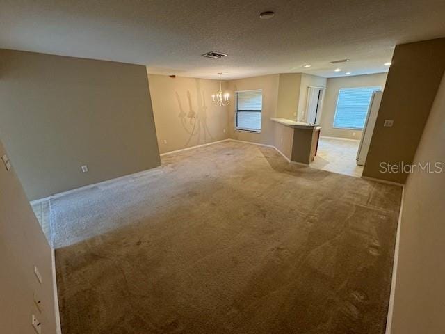 carpeted spare room featuring an inviting chandelier and a textured ceiling