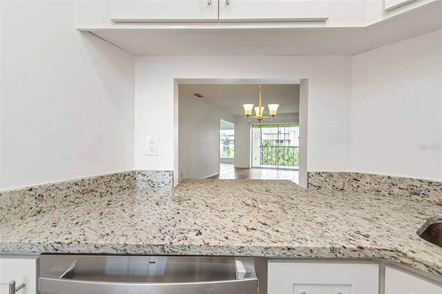 room details with a notable chandelier, white cabinets, and light stone counters