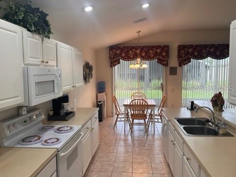 kitchen with a notable chandelier, white cabinets, white appliances, vaulted ceiling, and light tile patterned floors