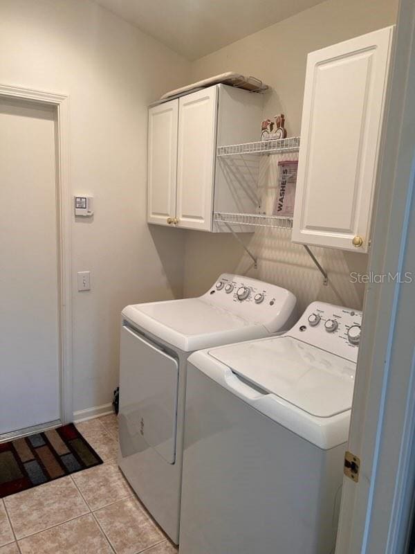 clothes washing area featuring cabinets, washer and dryer, and light tile patterned floors