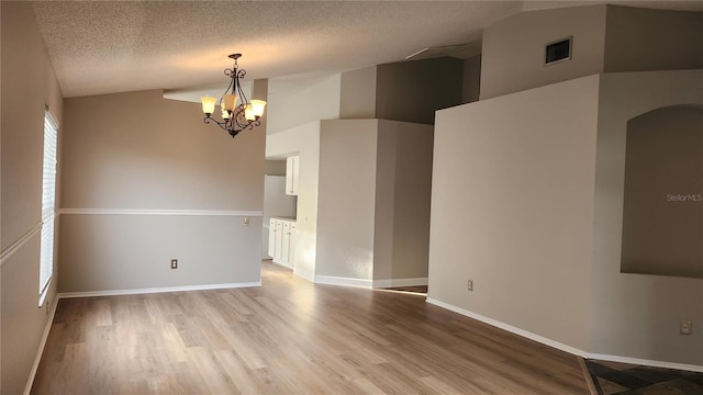 unfurnished room with vaulted ceiling, wood-type flooring, a textured ceiling, and an inviting chandelier