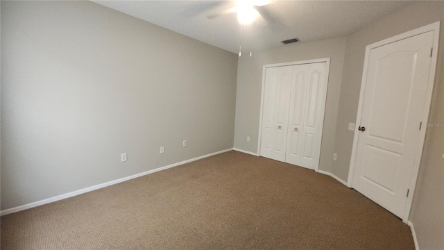 unfurnished bedroom with a closet, dark carpet, and ceiling fan