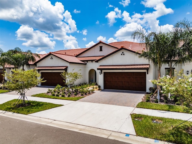 mediterranean / spanish-style house with a garage, decorative driveway, a tile roof, and stucco siding