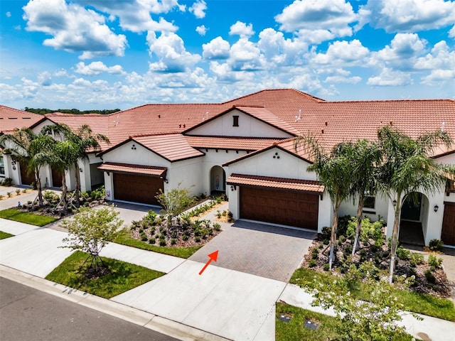 mediterranean / spanish house featuring decorative driveway, stucco siding, an attached garage, and a tiled roof