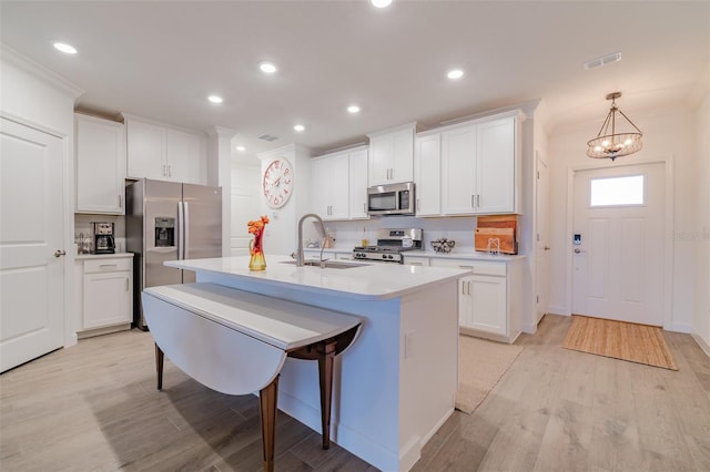 kitchen with appliances with stainless steel finishes, sink, hanging light fixtures, light hardwood / wood-style floors, and white cabinetry