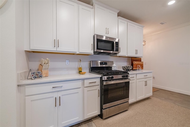 kitchen with white cabinetry, light hardwood / wood-style floors, appliances with stainless steel finishes, and ornamental molding