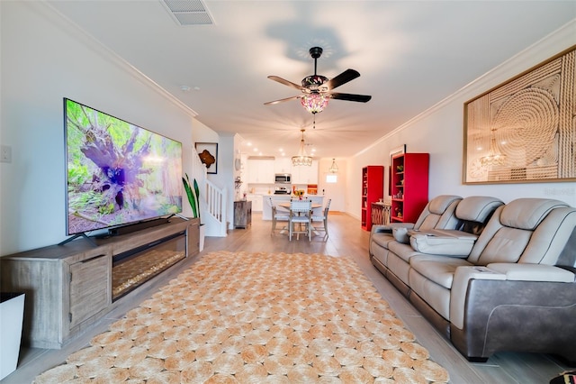 living room with light hardwood / wood-style floors, ceiling fan with notable chandelier, and crown molding