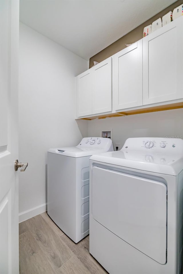 washroom featuring cabinets, light hardwood / wood-style flooring, and washing machine and dryer