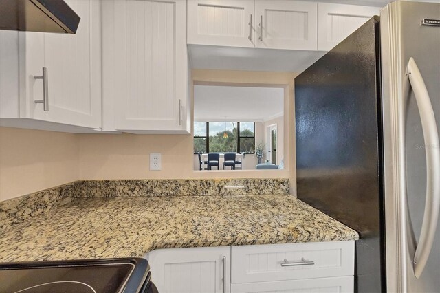 kitchen featuring range hood, light stone countertops, white cabinets, and stainless steel refrigerator