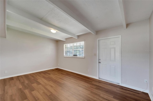 spare room featuring a textured ceiling, beam ceiling, and hardwood / wood-style floors