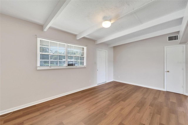 unfurnished room with beamed ceiling, wood-type flooring, and a textured ceiling