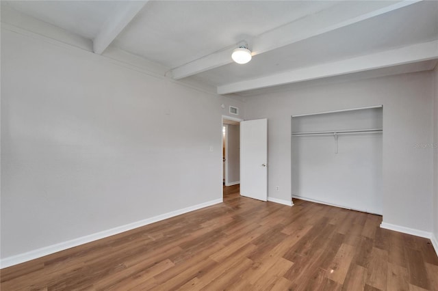 unfurnished bedroom featuring beamed ceiling, a closet, and hardwood / wood-style flooring