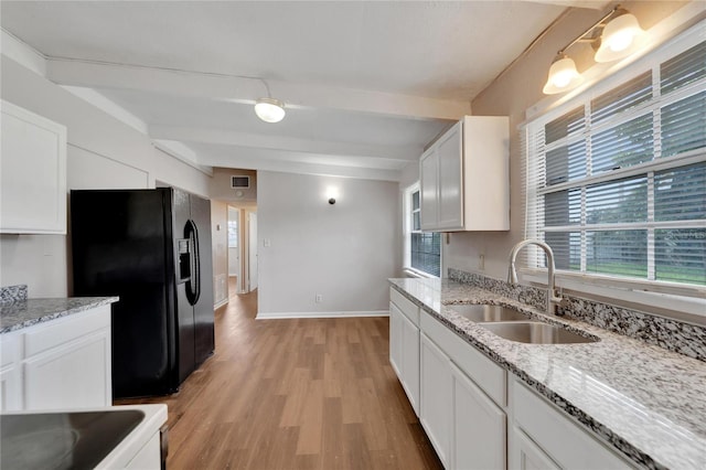 kitchen featuring white cabinetry, light wood-type flooring, light stone countertops, black fridge, and sink