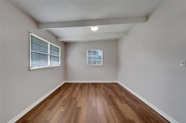 empty room featuring beamed ceiling, hardwood / wood-style floors, and a textured ceiling