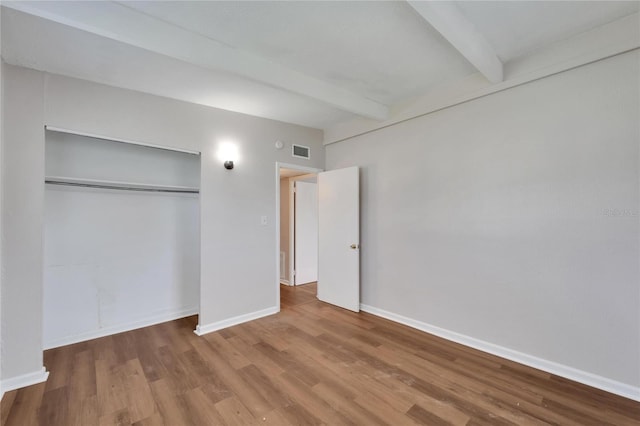 unfurnished bedroom featuring beamed ceiling, a closet, and hardwood / wood-style flooring