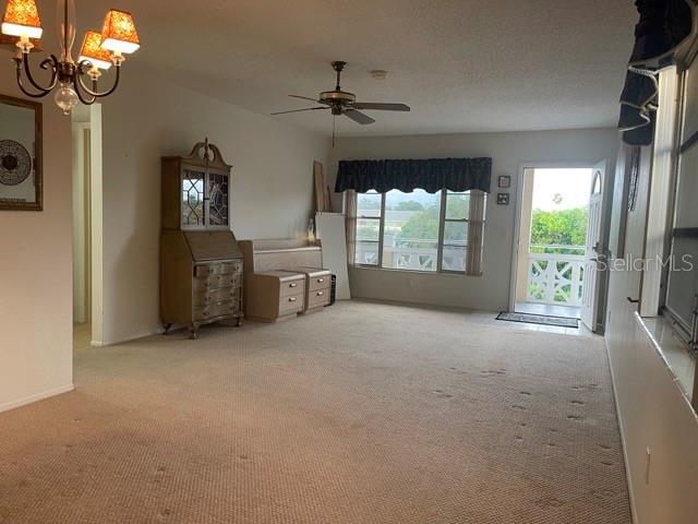 unfurnished living room featuring ceiling fan with notable chandelier and light colored carpet