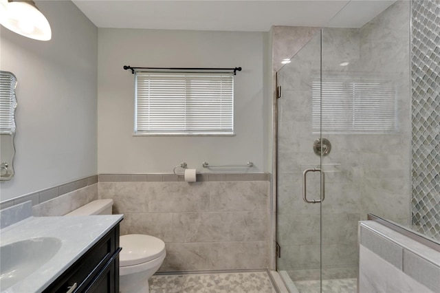 bathroom with tile walls, vanity, toilet, and a shower with door