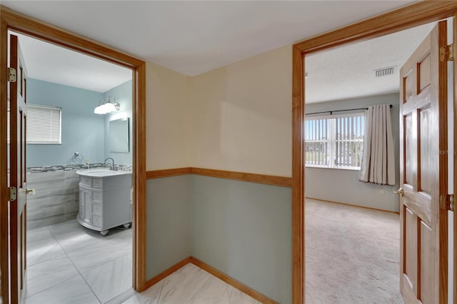 hallway featuring tile walls, sink, and light colored carpet