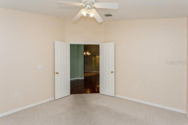 empty room featuring high vaulted ceiling, ceiling fan with notable chandelier, and hardwood / wood-style floors