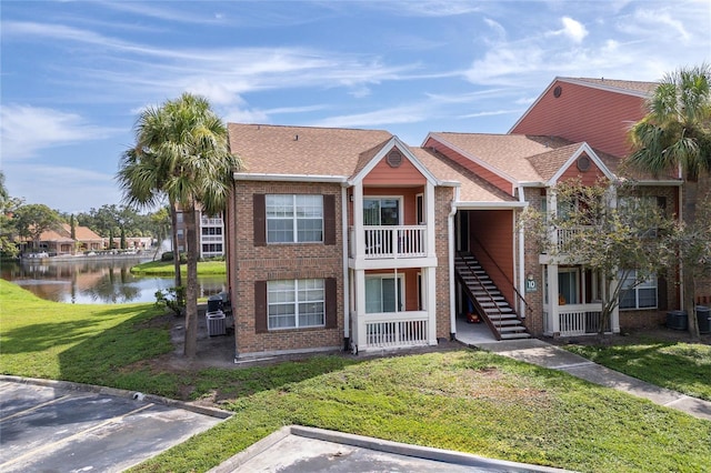 multi unit property featuring a water view, brick siding, stairway, and a front lawn