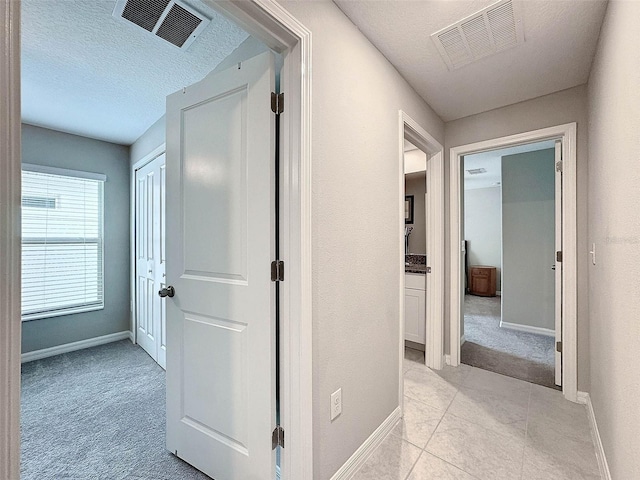 hallway with light carpet and a textured ceiling