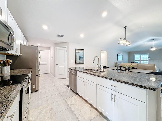 kitchen featuring stainless steel appliances, dark stone counters, sink, an island with sink, and white cabinetry