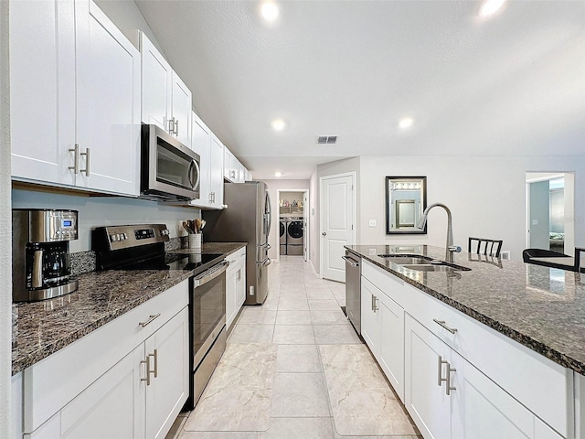 kitchen featuring stainless steel appliances, separate washer and dryer, dark stone countertops, and sink