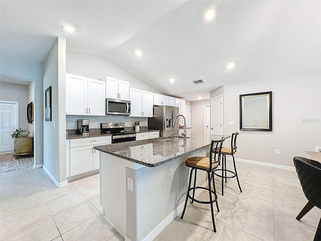 kitchen featuring vaulted ceiling, a kitchen island with sink, white cabinetry, appliances with stainless steel finishes, and dark stone countertops