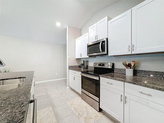 kitchen featuring stainless steel appliances, vaulted ceiling, light tile patterned flooring, white cabinetry, and dark stone countertops