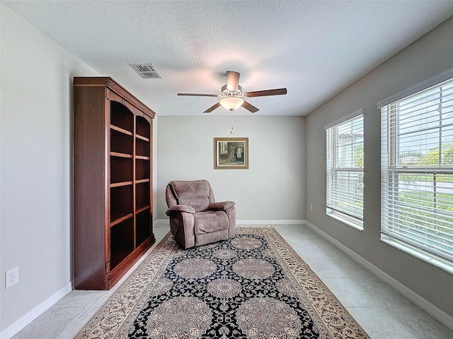 living area with a textured ceiling, light tile patterned floors, and ceiling fan