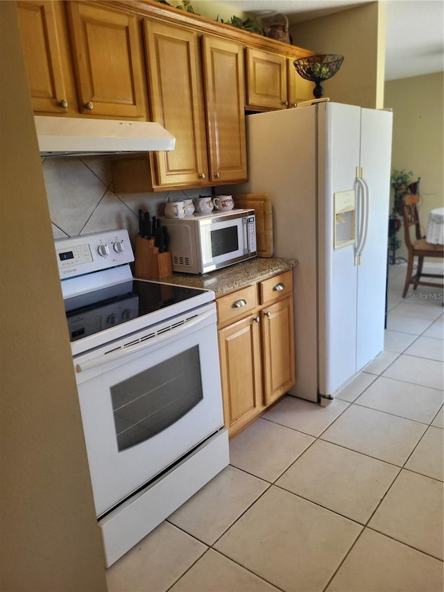 kitchen with dark stone countertops, light tile patterned floors, white appliances, and decorative backsplash