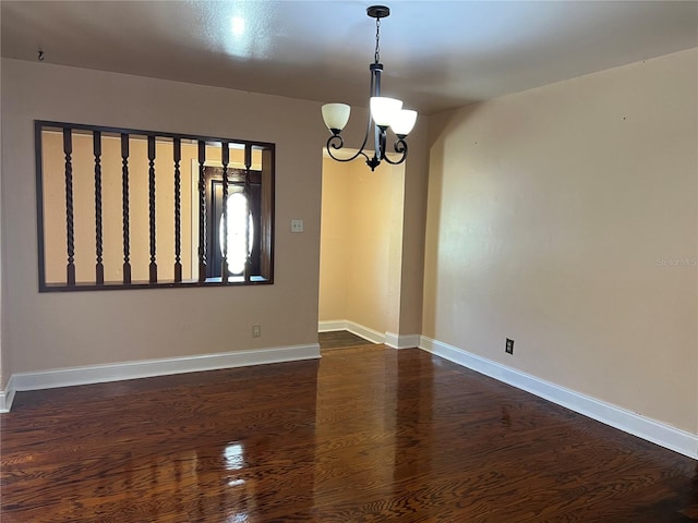 spare room with a notable chandelier and dark hardwood / wood-style flooring