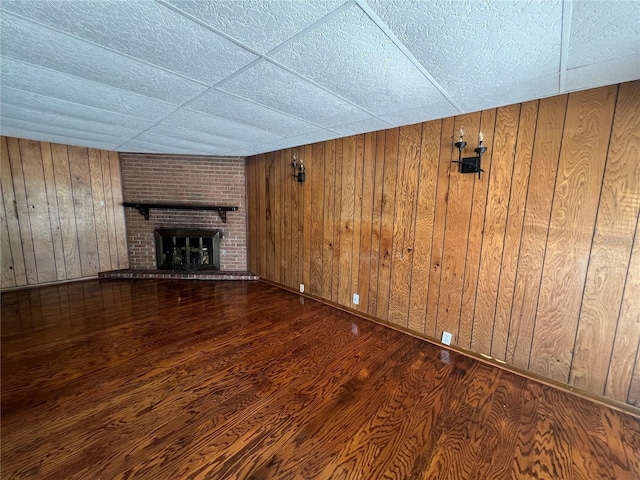 unfurnished living room with wooden walls, dark wood-type flooring, and a brick fireplace