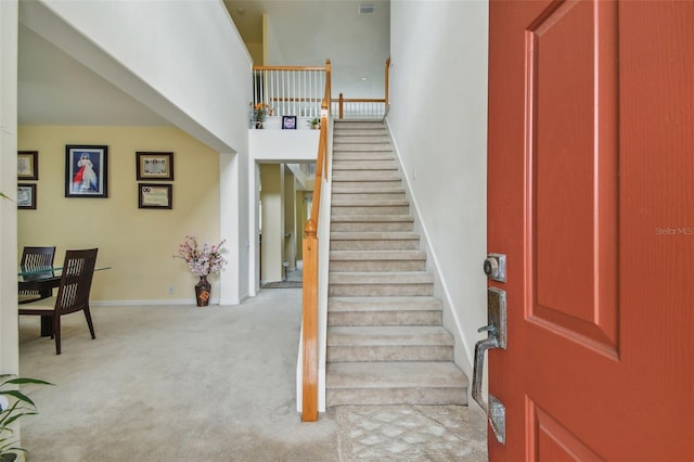 staircase featuring a towering ceiling, carpet, and baseboards