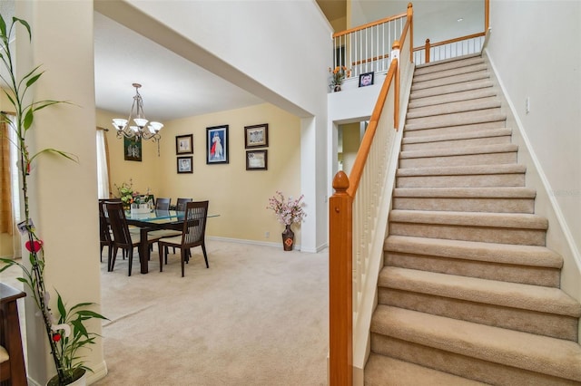 stairs with carpet flooring, a notable chandelier, a towering ceiling, and baseboards