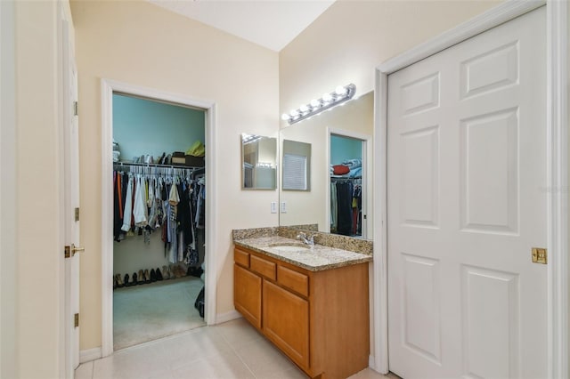 bathroom featuring a walk in closet, vanity, baseboards, and tile patterned floors