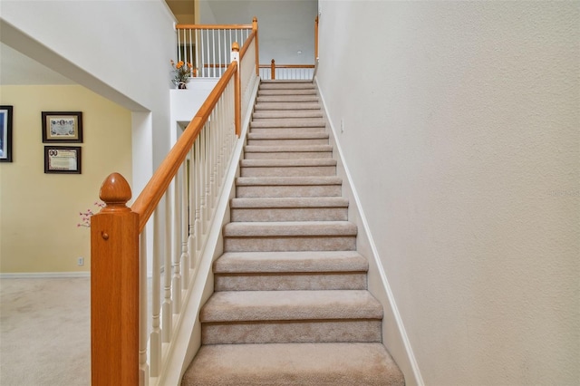 stairway featuring carpet floors, a high ceiling, and baseboards