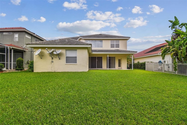 rear view of property with stucco siding, a lawn, a tiled roof, and fence