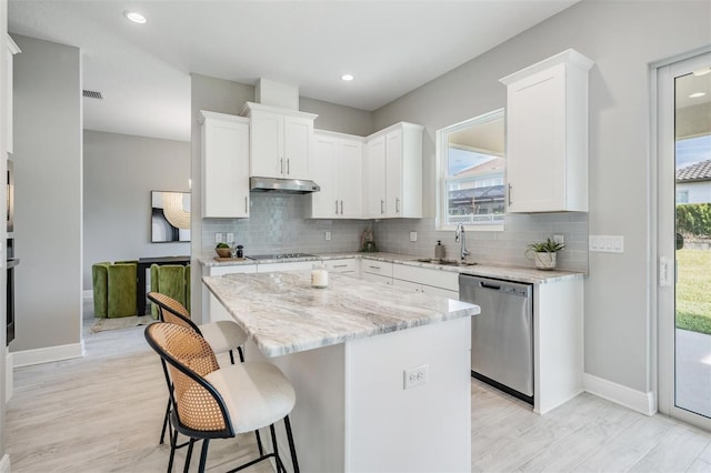 kitchen with light stone counters, stainless steel dishwasher, a kitchen island, sink, and white cabinetry