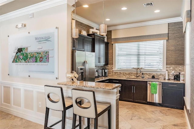 kitchen featuring light stone countertops, stainless steel appliances, crown molding, sink, and decorative light fixtures