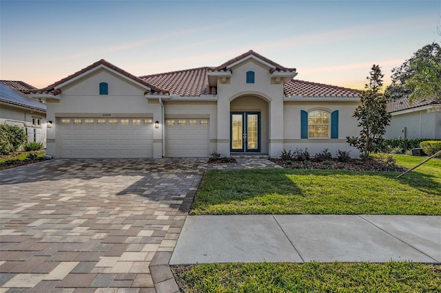 mediterranean / spanish-style home featuring a lawn, french doors, and a garage