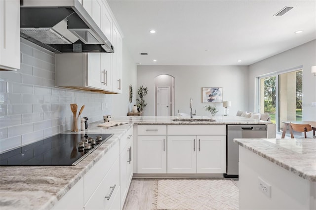 kitchen with light stone counters, black electric cooktop, sink, wall chimney range hood, and dishwasher