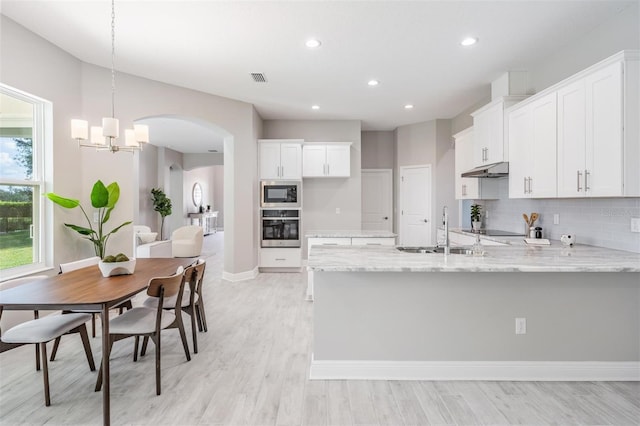 kitchen with built in microwave, stainless steel oven, hanging light fixtures, light stone counters, and white cabinets