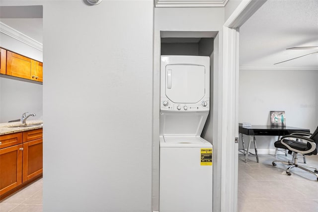 laundry area with light tile patterned flooring, stacked washer / dryer, crown molding, and sink