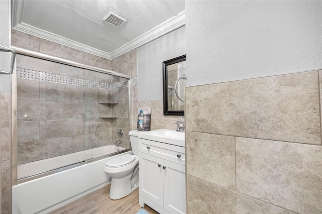 full bathroom with vanity, combined bath / shower with glass door, hardwood / wood-style flooring, ornamental molding, and tile walls