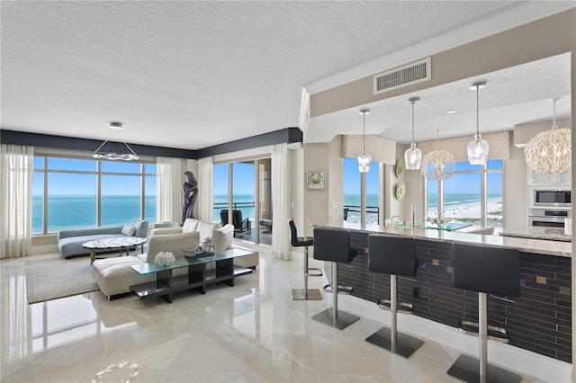 tiled living room featuring a water view, a wealth of natural light, a chandelier, and a textured ceiling