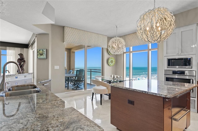 kitchen with light tile patterned floors, light stone counters, a chandelier, sink, and a kitchen island with sink