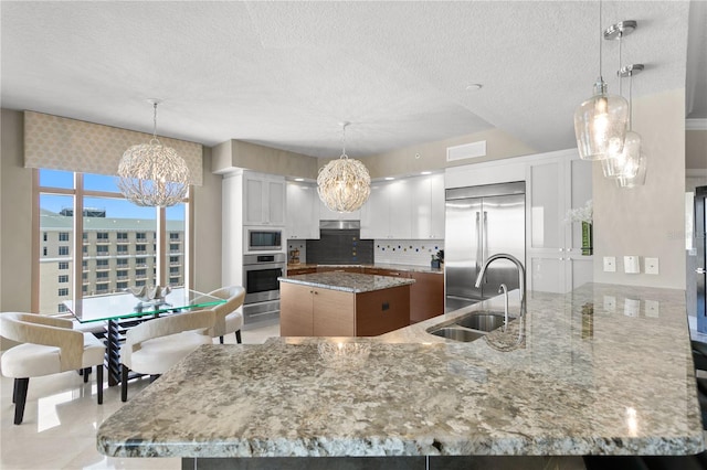 kitchen featuring built in appliances, backsplash, a center island, sink, and white cabinetry